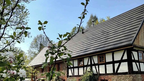 Ein traditionelles Fachwerkhäuschen mit geneigtem Dach, einem gepflegten Rasen und blauem Himmel.