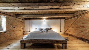 Ein rustikales Schlafzimmer im Dachgeschoss mit freiliegenden Holzbalken, einer Ziegelwand und einem Holzboden.