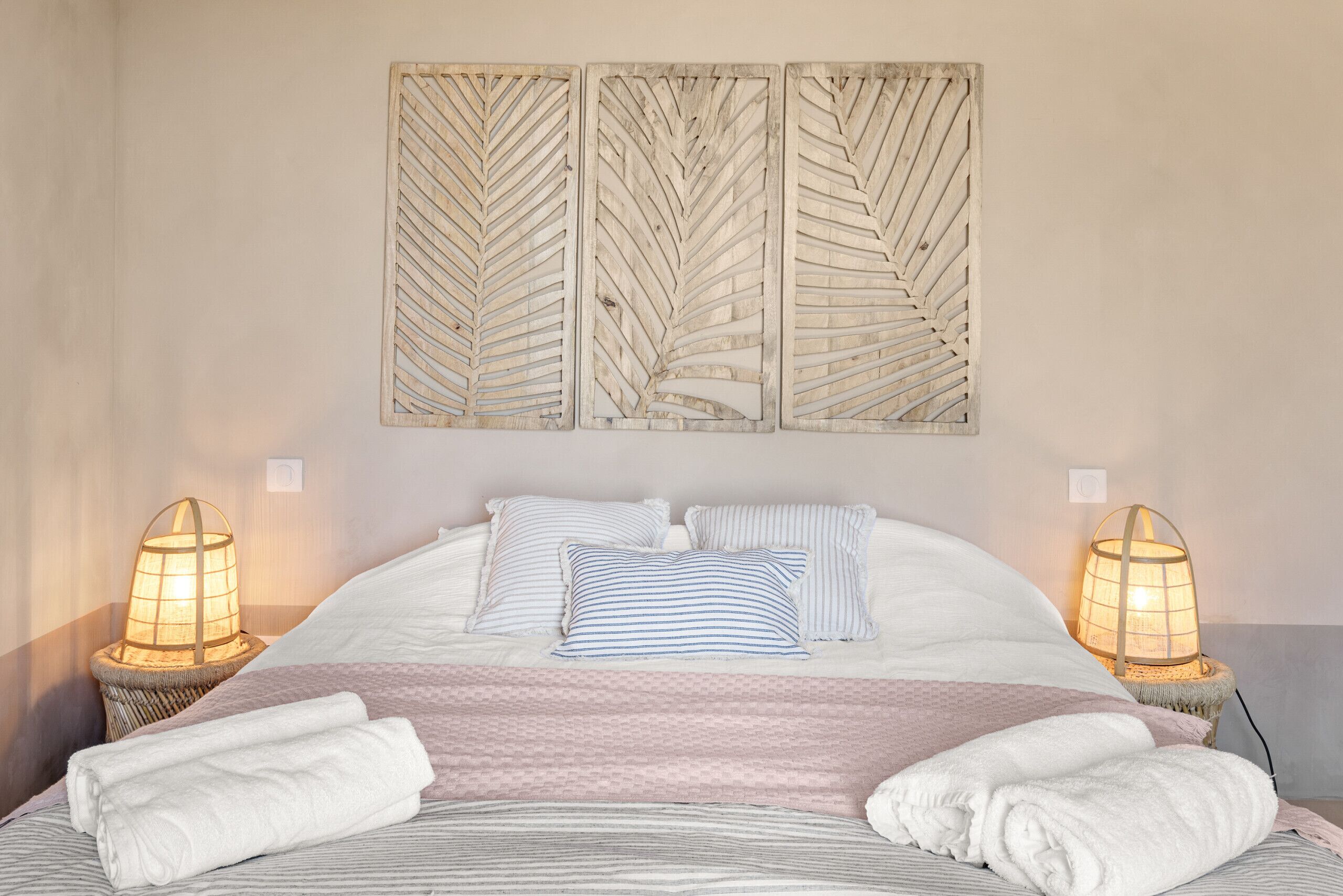 Ein ordentlich gemachtes Bett mit gestreiften Kissen, einer rosa Decke und zwei Nachttischlampen.
