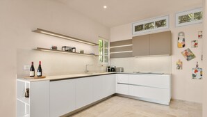 A modern kitchen with white cabinetry, a built-in island, and a window with a view. - Mas des Cigales – Pool & Saint-Paul views (Vence)