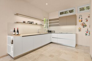 A modern kitchen with white cabinetry, a built-in island, and a window with a view. - Mas des Cigales – Pool & Saint-Paul views (Vence)