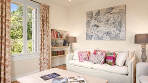 A living room with a white sofa, a coffee table with magazines, a bookshelf, and a large abstract painting on the wall. - Mas des Cigales – Pool & Saint-Paul views (Vence)
