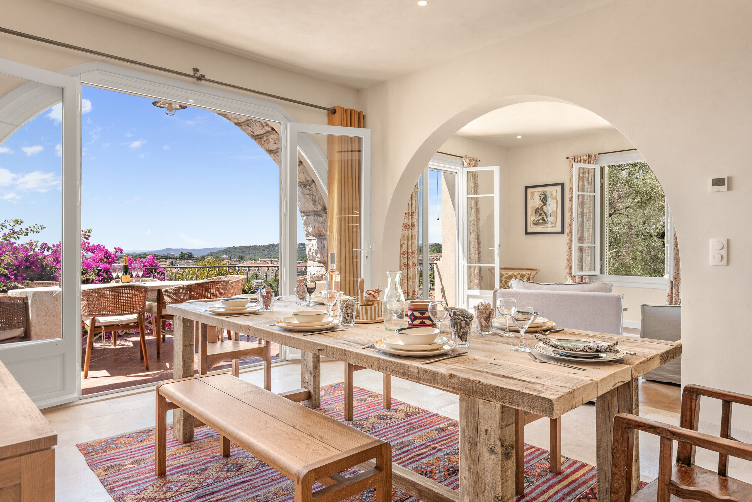 A dining area with a wooden table set for four, surrounded by chairs, with a view of the outdoors.