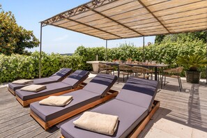 A rooftop terrace with sun loungers, a table, and chairs, surrounded by greenery. - Mas des Cigales – Pool & Village View (Vence)