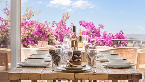 A table set with plates, glasses, and a bottle, with a view of pink flowers and a clear sky. - Mas des Cigales – Pool & Saint-Paul views (Vence)