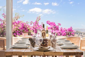 A table set with plates, glasses, and a bottle, with a view of pink flowers and a clear sky. - Mas des Cigales – Pool & Saint-Paul views (Vence)