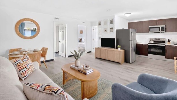 Ein modernes Wohnzimmer mit Sofa, Couchtisch und Fernseher. Direkt daneben befindet sich eine Küche mit Kühlschrank, Mikrowelle und Herd.