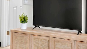 Ein Flachbildfernseher auf einem Holzboden, daneben eine Topfpflanze, an einer Wand mit gerahmten Bildern befestigt.
