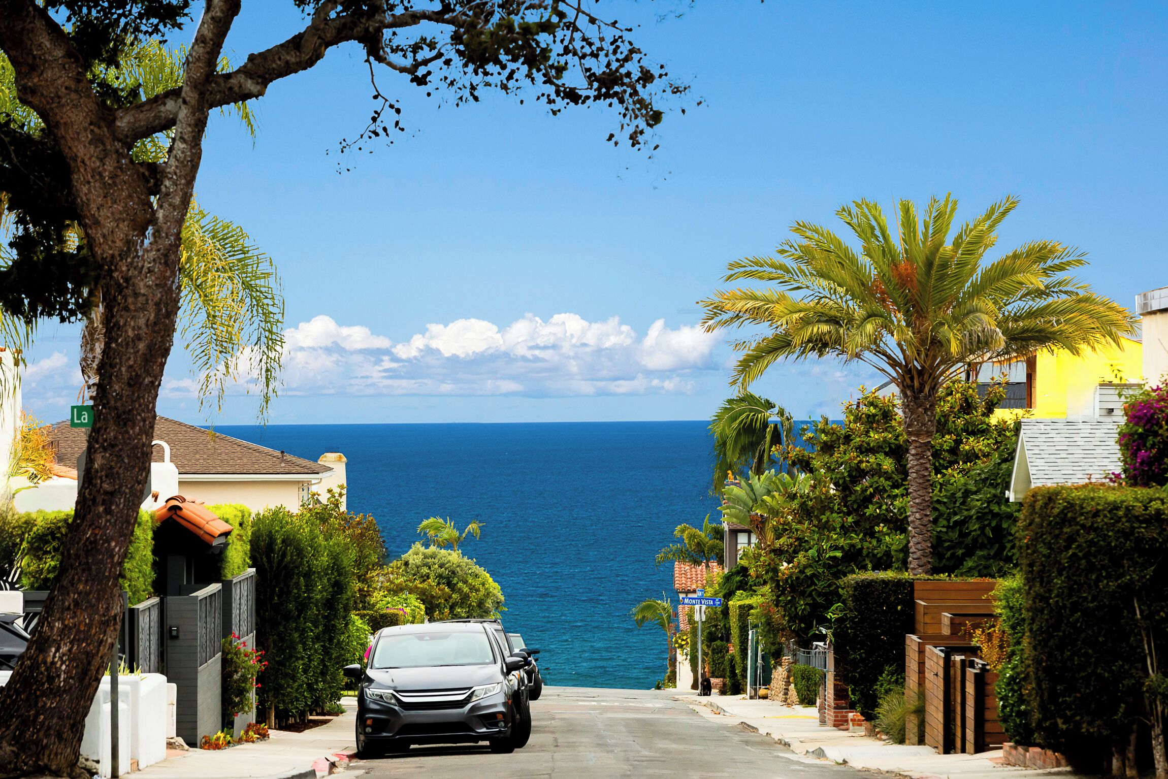 Uma rua costeira com um carro estacionado, casas e vista para o oceano.