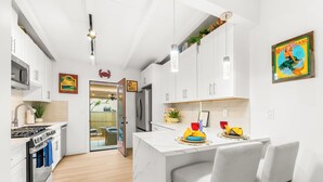 A modern kitchen with white cabinets, a marble island, and a dining area with chairs. - Walk To Beach and Village W/Jacuzzi & Firepit W/Great Reviews! (San Diego)