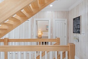 Un escalier en bois, doté d’une rampe, mène à une chambre à coucher qui contient un lit et une table de chevet.