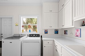 A laundry room with a washing machine, dryer, and a window with flowers. - 5BR Gulf-Front Home with Private Beach & Heated Pool ~ Sleeps 12 (Seacrest)