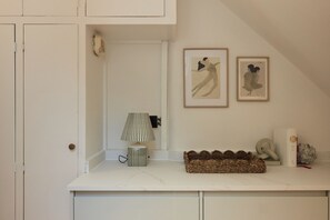 A bathroom with a white countertop, a striped lamp, framed artwork, and a woven basket. - Blythe & Bloom Garden Flat (London)