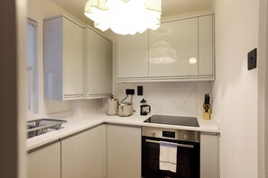 A modern kitchen with white cabinetry, a built-in oven, and a countertop with a coffee maker and kettle. - Blythe & Bloom Garden Flat (London)