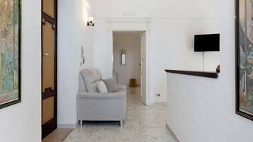 Ein Flur mit einer Couch, einem flachbildfernseher an der Wand und einer Tür zu einem anderen Zimmer.