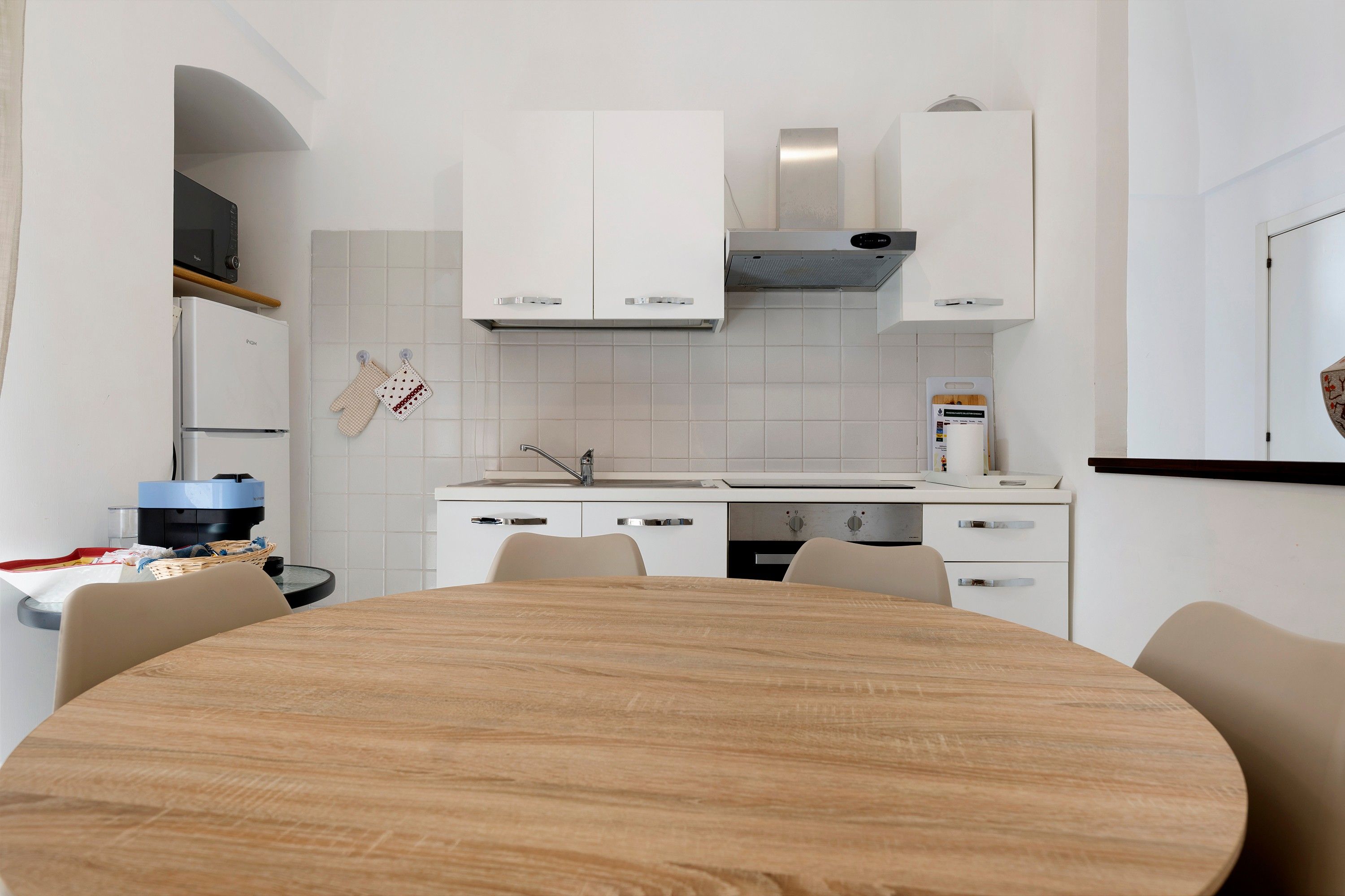 Eine moderne Küche mit weißen Schränken, einem runden Holztisch und einem eingebauten Backofen.