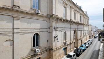 Eine Reihe geparkter Autos an einer Straße neben einem historischen Gebäude mit klassischer Architektur, das Rundbogenfenster und dekorative Stuckarbeiten aufweist.