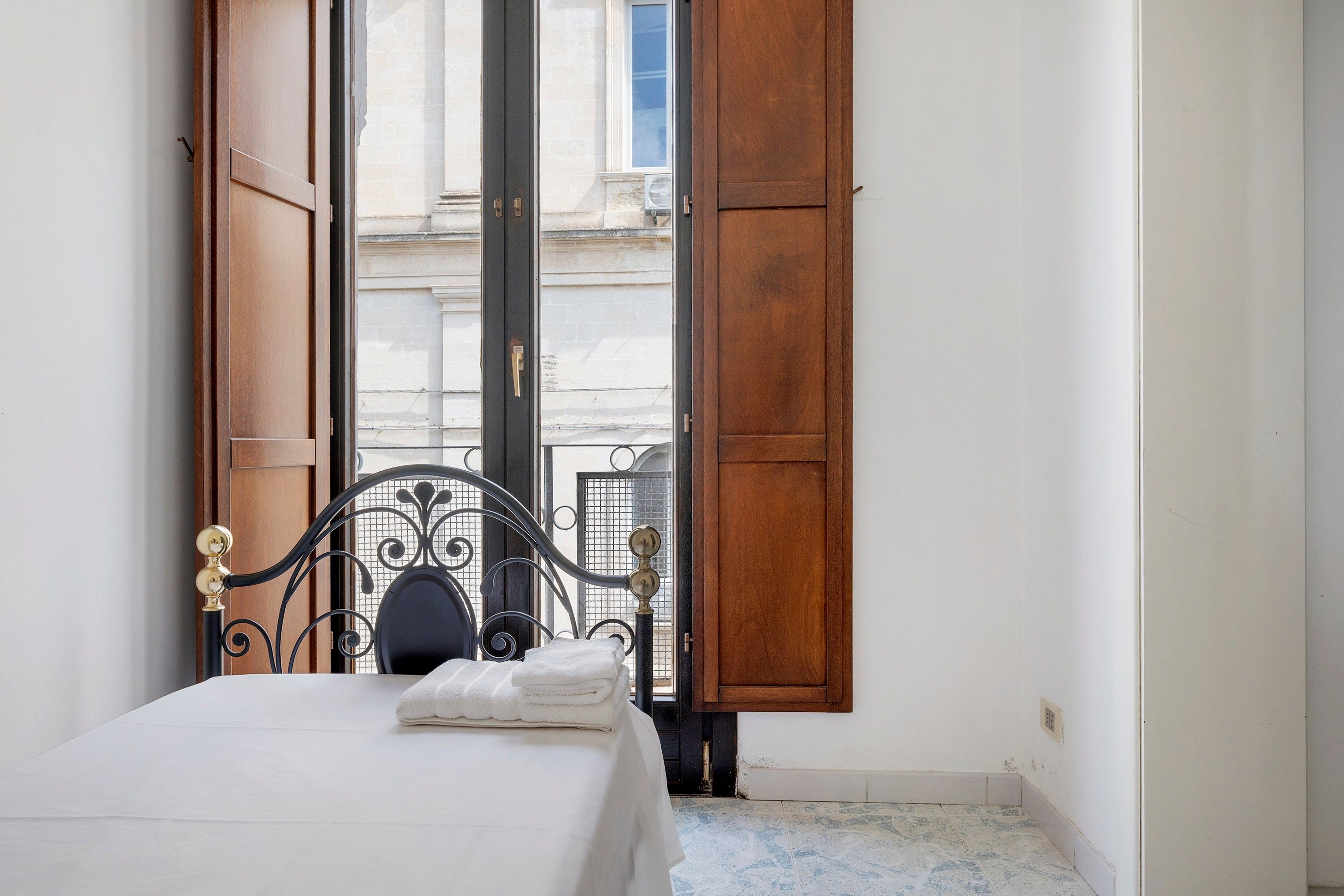 Ein Hotelzimmer mit einem Bett, einem Fenster mit Holzjalousien und Blick auf ein Gebäude.