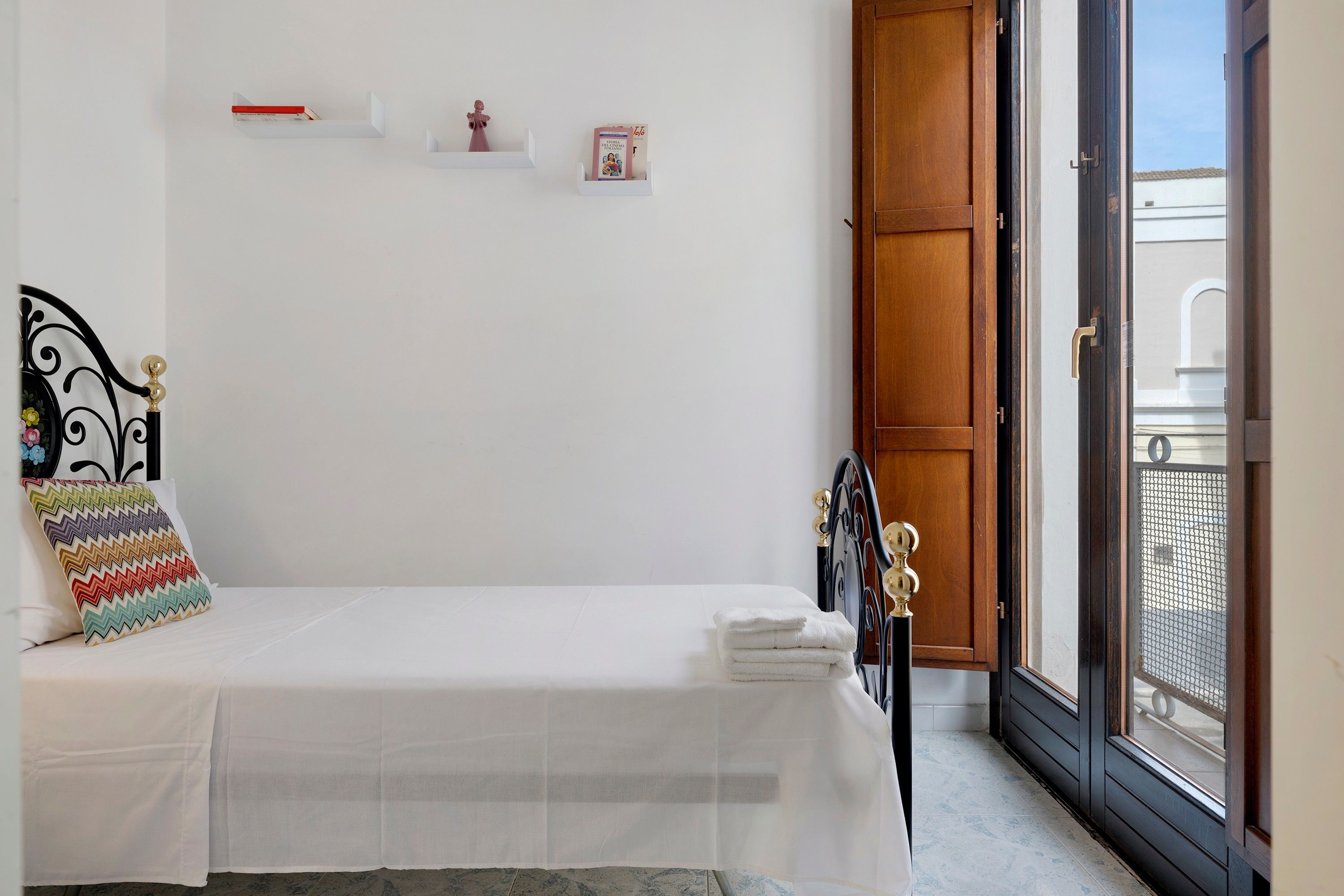 A bedroom with a bed, a window, and a door leading to an outdoor balcony.