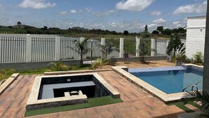 A swimming pool with a stone border, a small hot tub, and a fenced area with palm trees. - The Embassy Boutique Apartment (Jos)