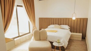A bedroom with a bed, a chair, a bedside table, and a window with curtains. - The Embassy Boutique Apartment (Jos)