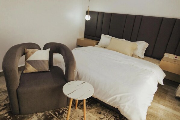 Un dormitorio con cama, una silla, una mesita redonda y una mesita de noche.