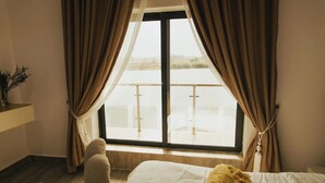 A hotel room with a bed, a window with curtains, a view of a balcony, and a small table with a plant. - The Embassy Boutique Apartment (Jos)