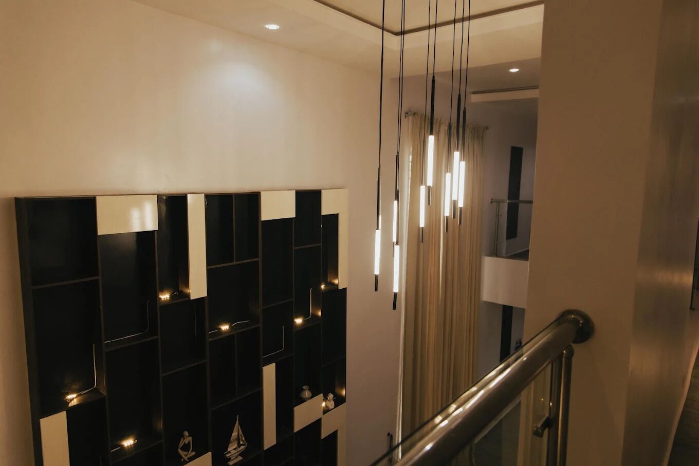 Um interior moderno com parede estampada em preto e branco, escada com corrimão de vidro e iluminação pendente.