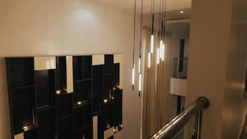 Um interior moderno com parede estampada em preto e branco, escada com corrimão de vidro e iluminação pendente.