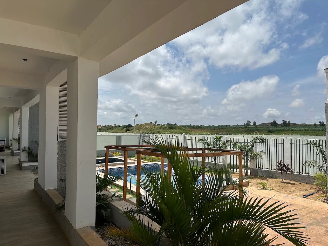Un espacio al aire libre techado con piscina, palmeras y vistas a un campo.