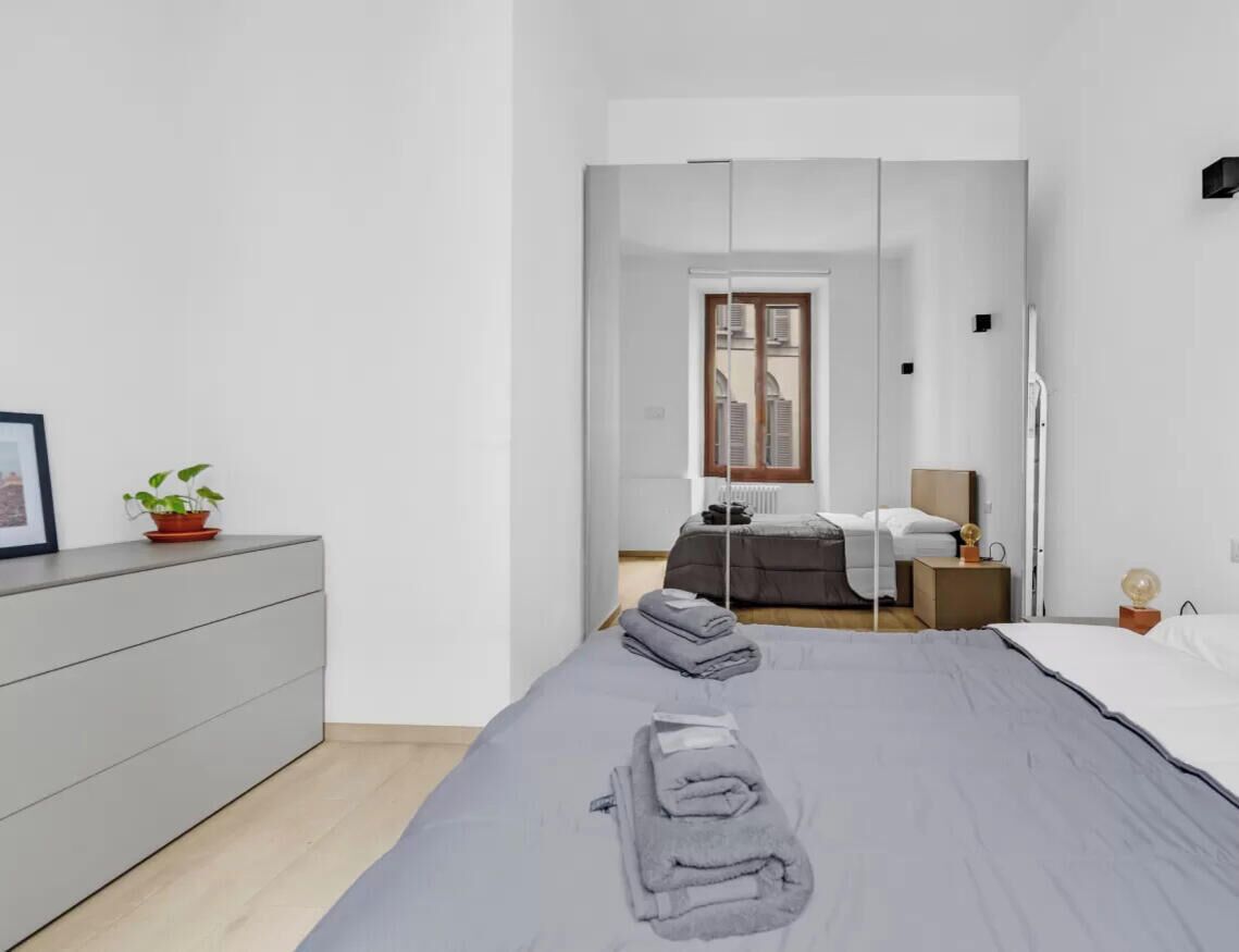 Une chambre à coucher moderne, avec un lit, une table de chevet et une vue sur une autre pièce grâce à une porte vitrée.