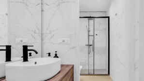 Une salle de bain avec un mur en marbre blanc, un meuble-lavabo en bois, un robinet noir et une douche à parois de verre.