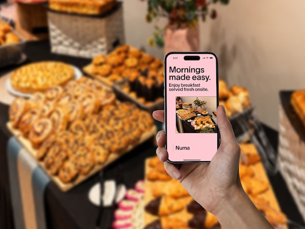 A hand holding a smartphone displaying a breakfast menu with various pastries.