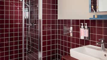 A bathroom with a glass-enclosed shower, a white sink, and red tiled walls.