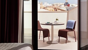 A room with a bed, a balcony with two chairs, a table, and a view of buildings. - Numa Valencia Sant Agustí (València)