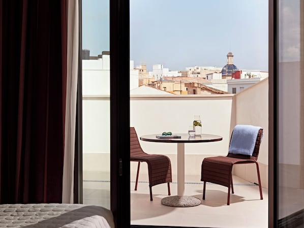 Una habitación con cama, un balcón con dos sillas, una mesa y vista a edificios.