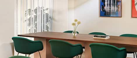 A conference room with a long table, six green chairs, a vase with flowers, and two artworks on the wall.