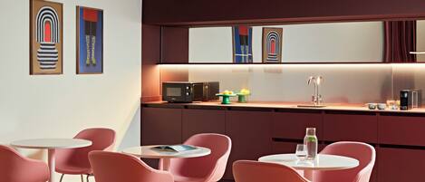 Una cocina moderna con microondas, lavamanos y zona de comedor con sillas rosadas.