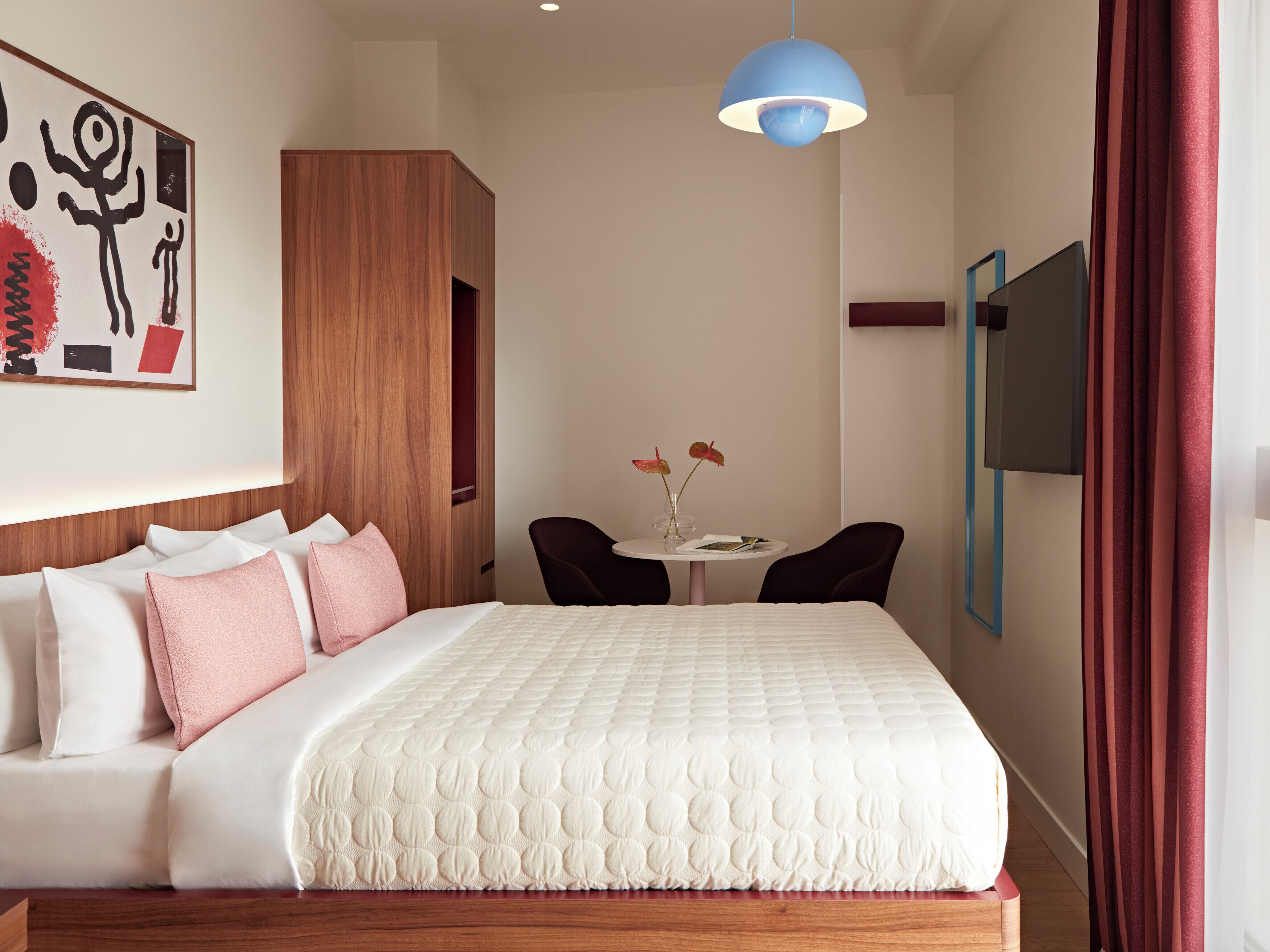 Een hotelkamer met een bed, een bureau, een stoel, een televisie en kunst aan de muur.