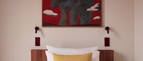 A neatly made bed with white and mustard-colored pillows, a quilted white mattress, and a wall-mounted artwork above.