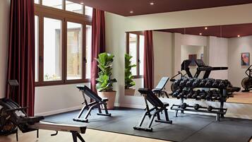 Un gimnasio con equipo de ejercicio, ventanas amplias y plantas en macetas.