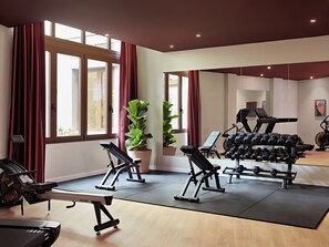 Un gimnasio con equipo de ejercicio, ventanas amplias y plantas en macetas.