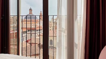 A hotel room with a large window overlooking a cityscape with historical buildings.