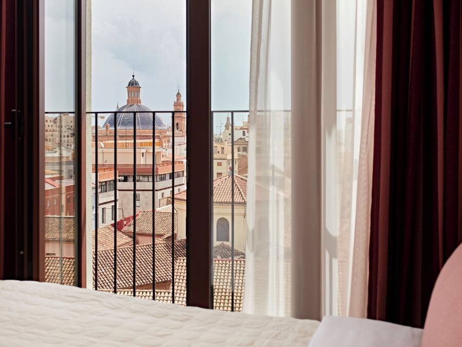 Una habitación de hotel con un ventanal grande con vistas a un paisaje urbano que incluye edificios históricos.