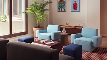 Una sala de estar moderna con dos sillones azules, un reposapiés marrón, una planta grande en maceta y obras de arte en la pared.