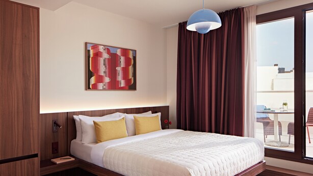 A hotel room with a large bed, a nightstand, a wooden wardrobe, a window with curtains, and a ceiling light. - Numa Valencia Sant Agustí (València)