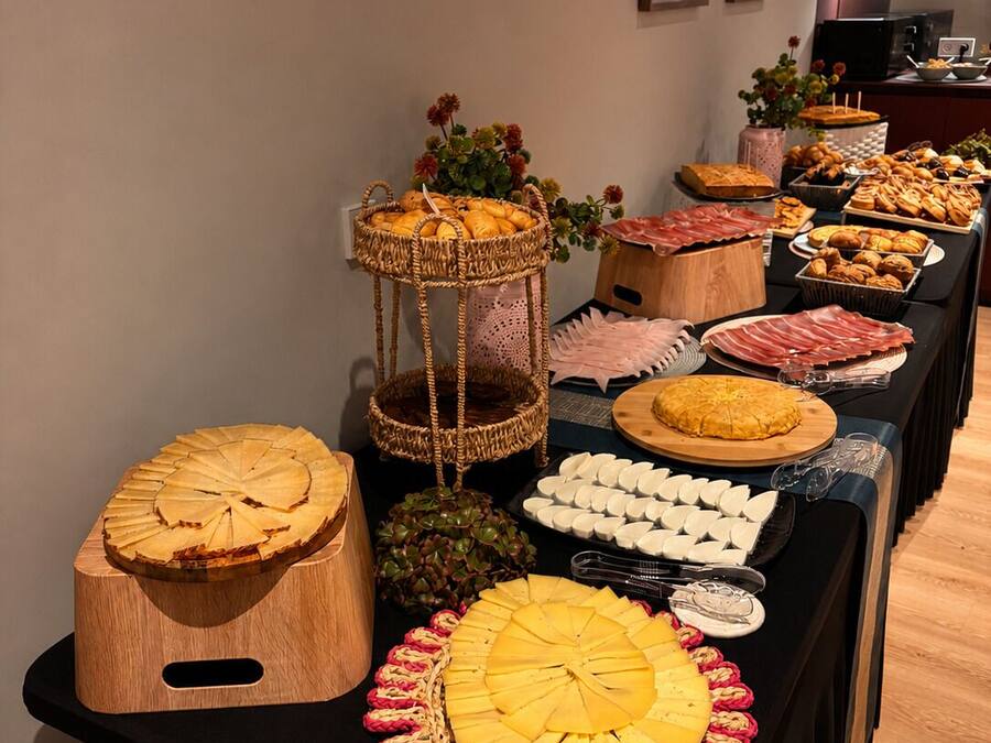 Una taula de buffet amb diversos plats, incloent-hi una gran taula de tallera de fusta amb un dibuix circular, una cistella amb flors i una safata d'articles rodons blancs.