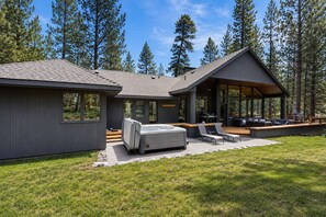 A modern house with a hot tub, outdoor seating, and a deck overlooking a forest. - Luxury 5BR Forest Retreat at Black Butte Ranch (Sisters)