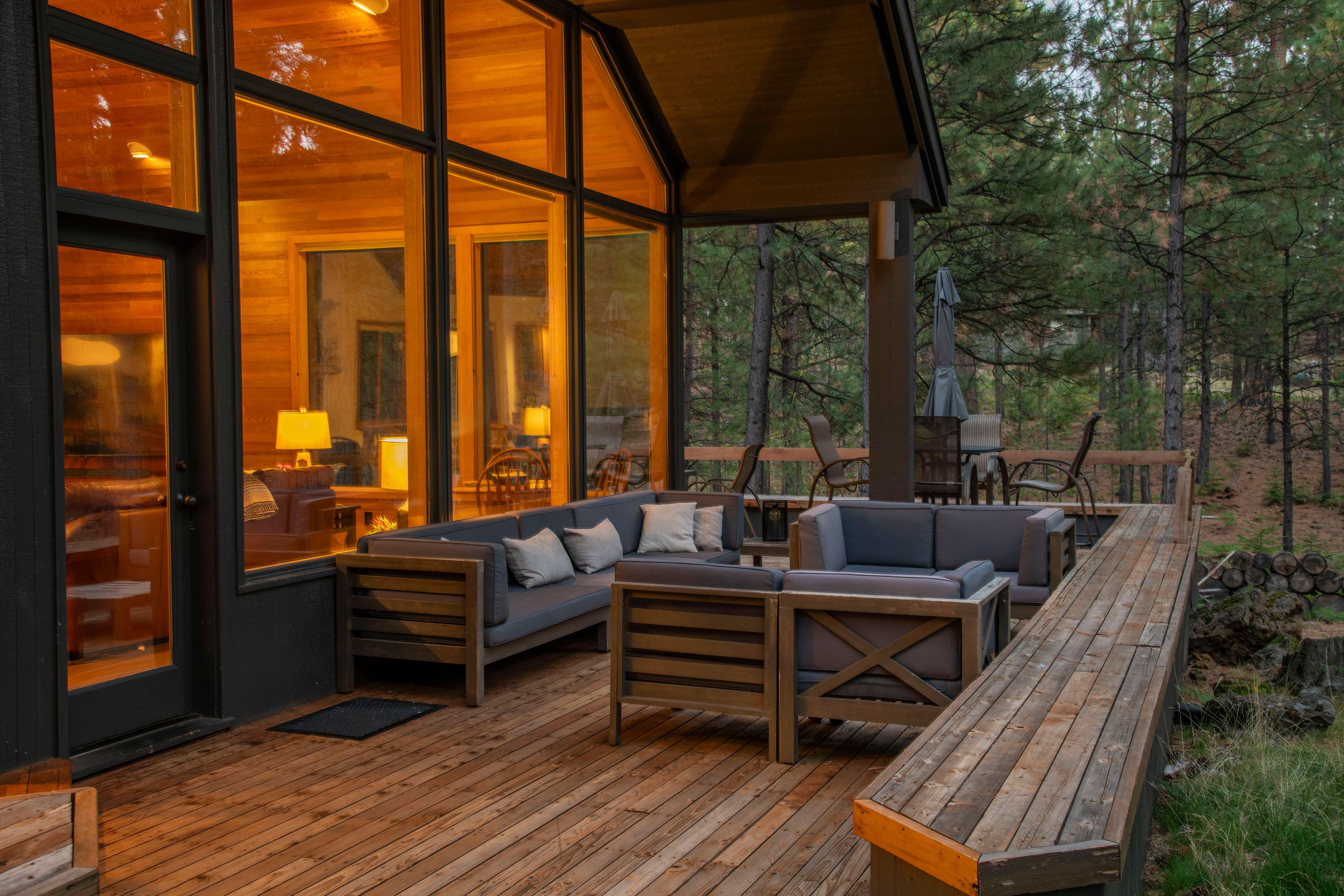 A wooden deck with outdoor furniture, including sofas and chairs, and a covered seating area with a view of the surrounding forest.