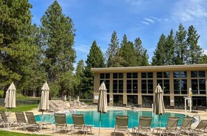 A pool area with lounge chairs and umbrellas, surrounded by trees and a building with large windows. - Luxury 5BR Forest Retreat at Black Butte Ranch (Sisters)